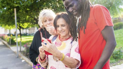 Three friends sharing a joyful moment looking at a smartphone in the park.