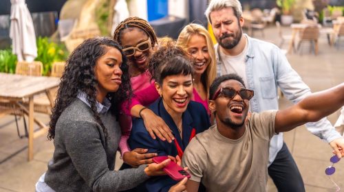 Happy group of multiracial friends taking selfie at night party in the terrace of a bar