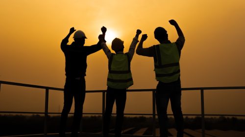 Rear view of group of engineer team look at sunset at solar cell field. Attractive technician worker working on roof, maintenance and check solar cell panels equipment box of photovoltaic panel system
